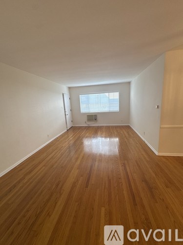A spacious room with wooden floors and a sliding glass door leading to a balcony.