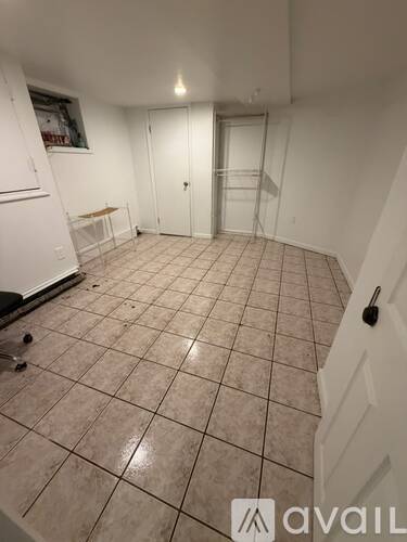 A room with white walls and tiled flooring with a door and a cabinet.