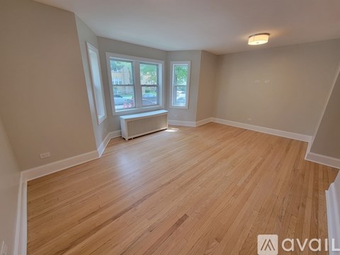 A spacious room with wooden flooring and a window with a view of a street.