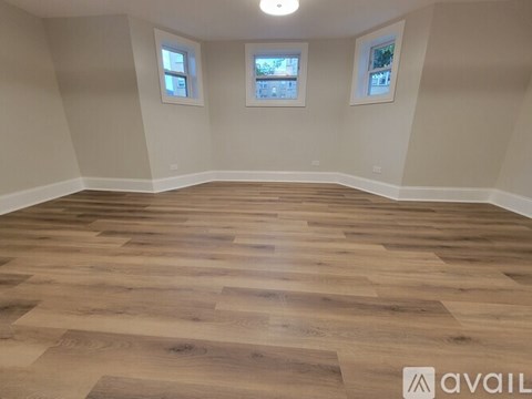 A room with wooden flooring and two windows.