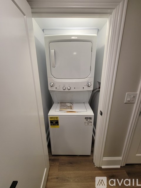 A white dryer is in a small space between a wall and a cabinet.