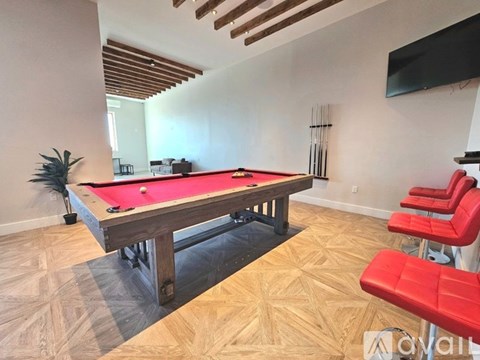 A pool table with red seating is in the foreground of a room with wooden flooring and a ceiling with exposed beams.