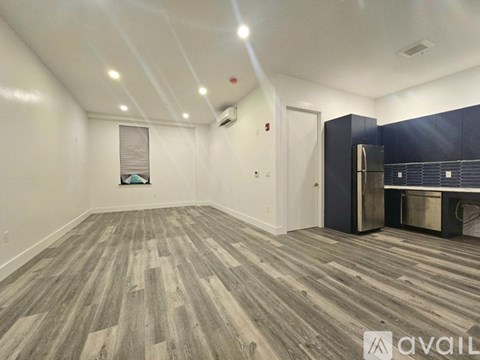 A spacious room with wooden flooring and a kitchenette in the corner.