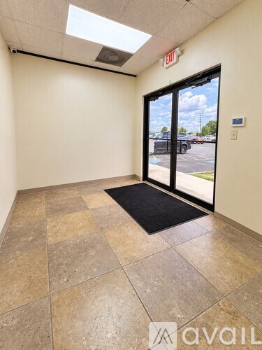 A hallway with a tiled floor and a black mat in front of a glass door.