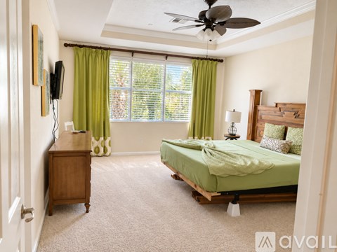 A bedroom with a bed, dresser, and window with green curtains.