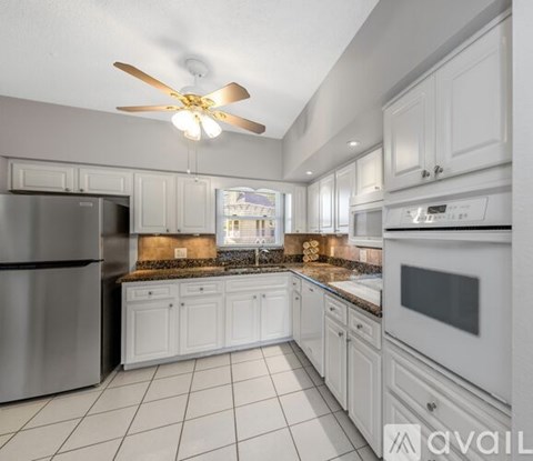 A kitchen with white cabinets and appliances, a ceiling fan, and a view of a cityscape through a window.
