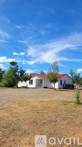 A white house with a red roof stands alone in a dry, brown field.