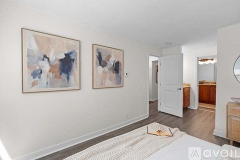 A bedroom with a white bed and two abstract paintings on the wall.
