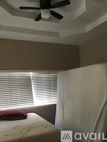 A bedroom with a bed, a ceiling fan, and a window with blinds.