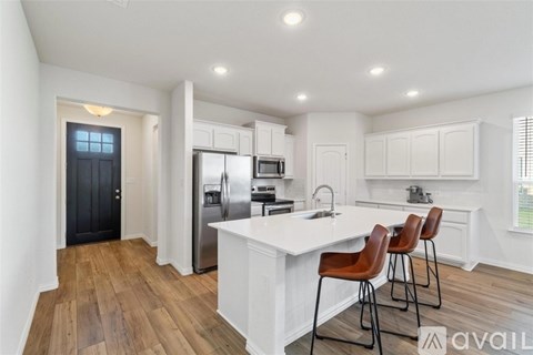 A kitchen with white cabinets and a white island with brown chairs.