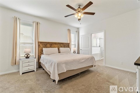 A bedroom with a large bed, a ceiling fan, and a nightstand with a lamp.