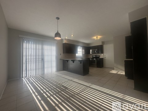 A sunlit kitchen with a black fridge and white cabinets.