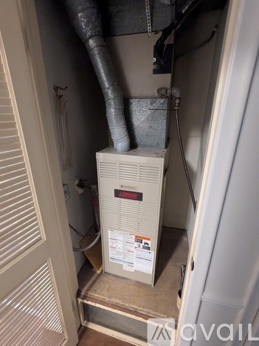 A white furnace is in a narrow space under a staircase.
