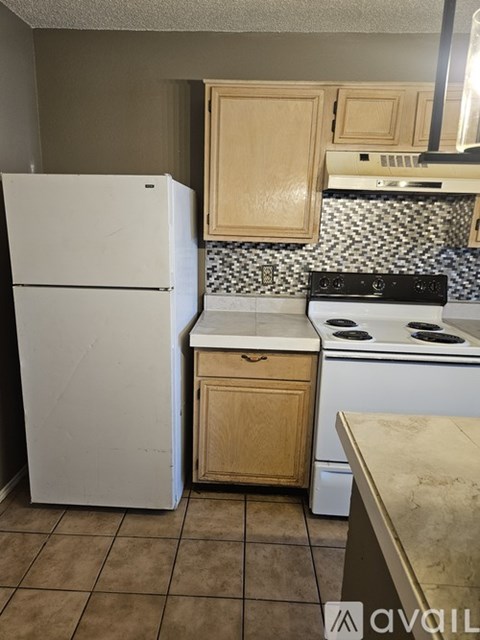 A kitchen with a white fridge, wooden cabinets, and a black and white tiled backsplash.