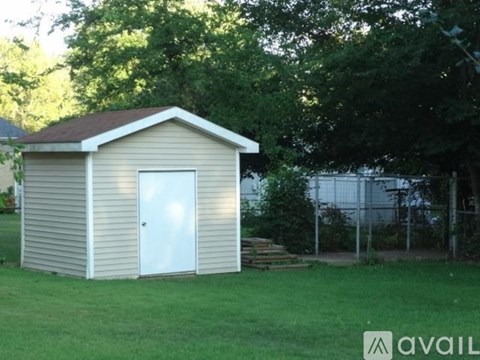 A small building with a white door is surrounded by greenery.