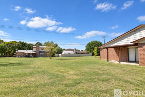 A grassy field with a house and trees in the background.