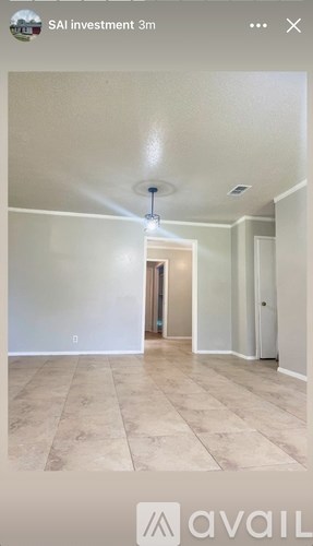A spacious room with beige tiled flooring and white walls, with a doorway leading to another room.