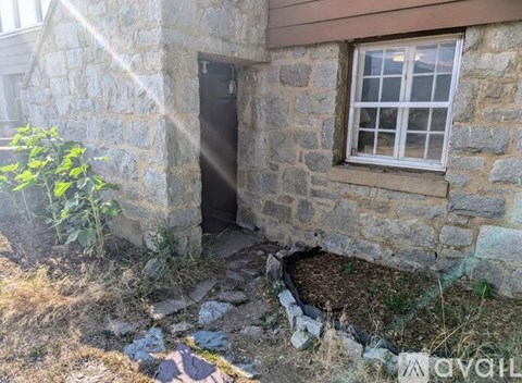 A stone building with a window and door, surrounded by a small garden.