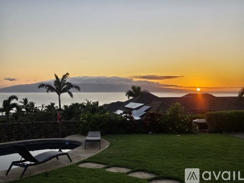 A sunset view from a backyard with a pool and patio furniture.