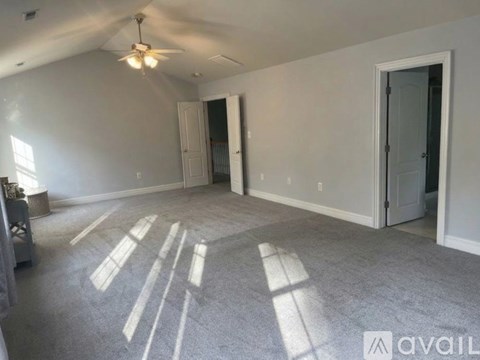 A spacious room with a ceiling fan and sunlight streaming in through the windows.