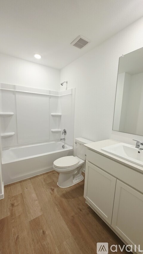 A white bathroom with wooden flooring and a white toilet.