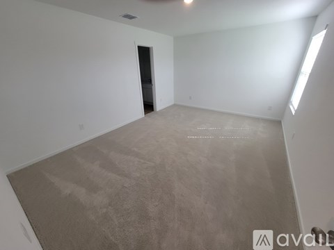 A spacious room with a carpeted floor and a door on the left side.