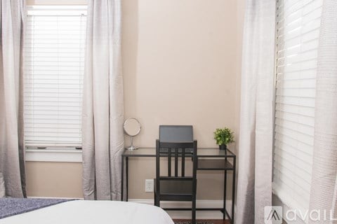 A bedroom with a bed, a desk with a laptop, and a window with curtains.