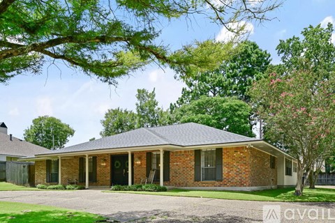A house with a brick exterior and a black roof is surrounded by greenery.