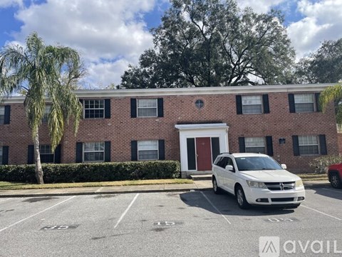 A white car is parked in a parking lot in front of a brick building.