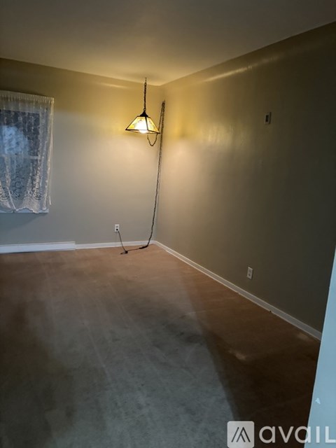 A room with a hanging light fixture and a window with curtains.