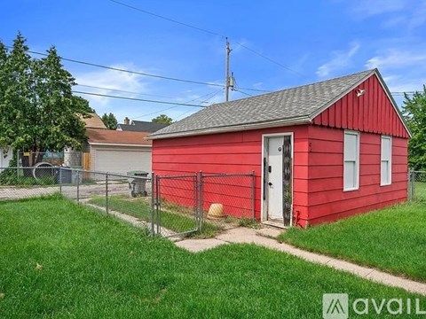 A red barn with a white door and windows is surrounded by a fence and green grass.