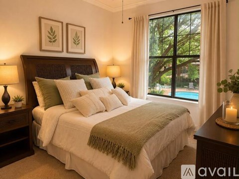 A bedroom with a large bed and a view of a pool through the window.