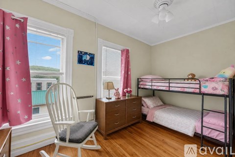 A bedroom with a bunk bed, a chair, and a window with curtains.