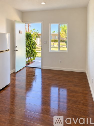 A room with a white fridge and wooden floors.