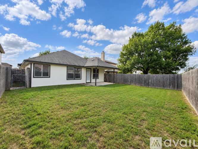 A house with a white exterior and a grey roof is surrounded by a wooden fence and has a green lawn.