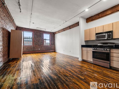 A spacious kitchen with wooden floors and a brick wall.