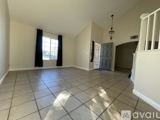 A spacious room with tiled flooring and a large window with curtains.