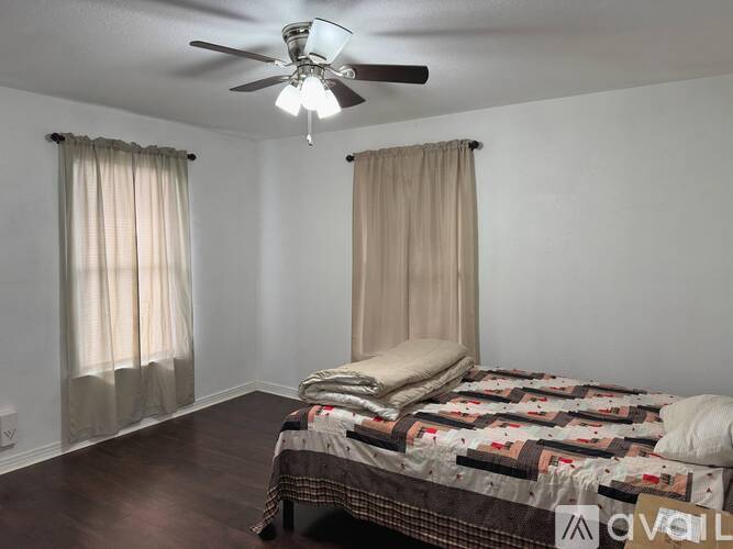 A bedroom with a bed, a ceiling fan, and two windows with curtains.
