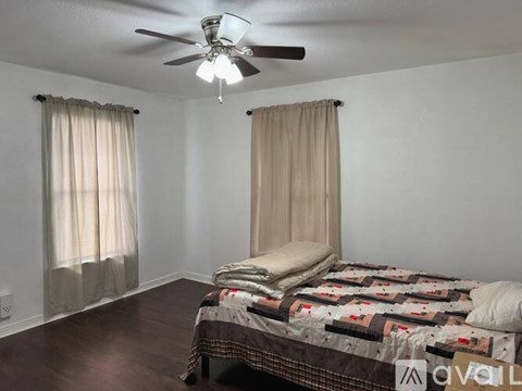 A bedroom with a bed, a ceiling fan, and two windows with curtains.