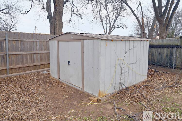 A shed sits in a backyard with a fence and trees in the background.