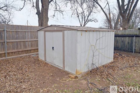 A shed sits in a backyard with a fence and trees in the background.