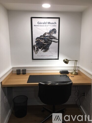 A poster of Gerald Musch is hanging on the wall above a desk with a black chair and a black trash can.