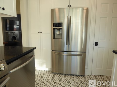 A stainless steel refrigerator in a kitchen with black and white tiled flooring.