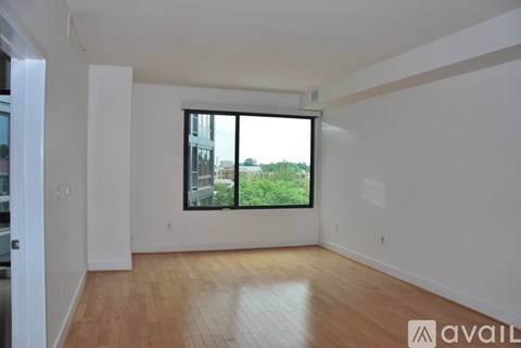 A spacious room with wooden flooring and a large window overlooking a green landscape.