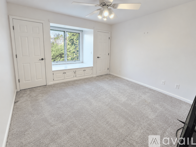 A room with a carpeted floor, a ceiling fan, and a window with a view of trees outside.