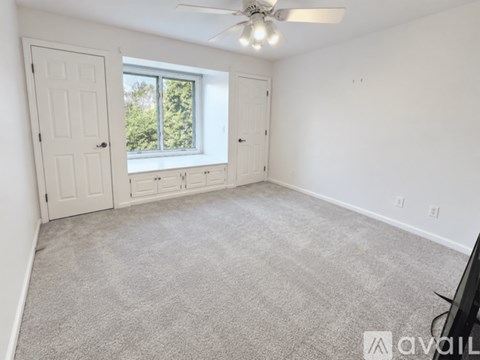 A room with a carpeted floor, a ceiling fan, and a window with a view of trees outside.