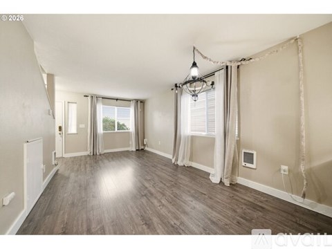 A spacious room with wooden flooring and a chandelier hanging from the ceiling.