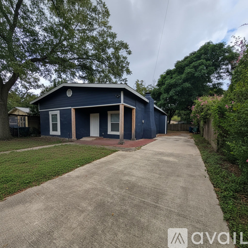 A blue house with a white door and windows is surrounded by greenery.