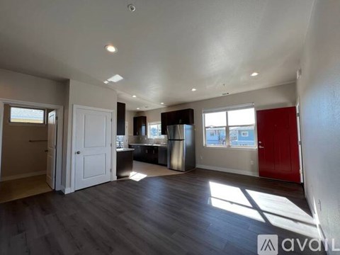 A spacious room with wooden floors and a red door.