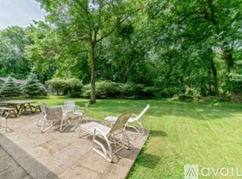 A patio with chairs and a table is surrounded by trees.